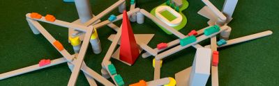 The board game Tokyo Highway at the end of the game with multiple gray sticks, with vehicles on them, balanced on grey or yellow towers and several coloured wooden pieces acting as city buildings. On a green beige table cover.