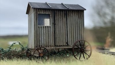 A model of a small weather beaten shepherds hut with rusted iron wheels.