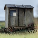A model of a small weather beaten shepherds hut with rusted iron wheels.